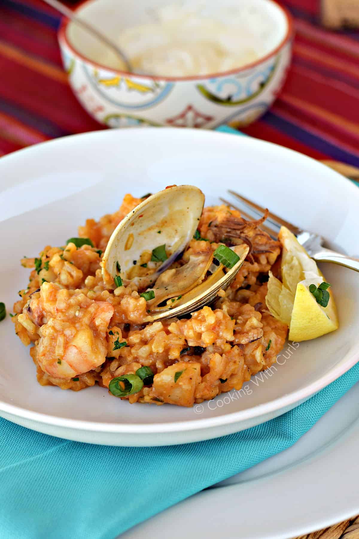 A serving of Seafood Paella with an open clam and baby octopus on a small plate with a lemon wedge on the side.