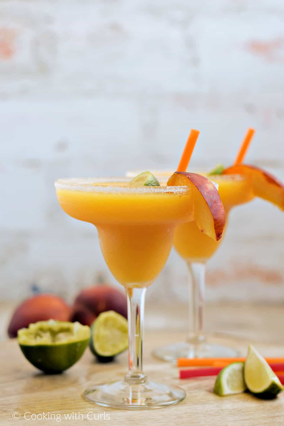 Two frozen peach margaritas with lime and peach slices as garnish.