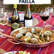 Seafood and rice in a large paella pan outside on a striped tablecloth surrounded by wine bottles and salad with title graphic across the top.