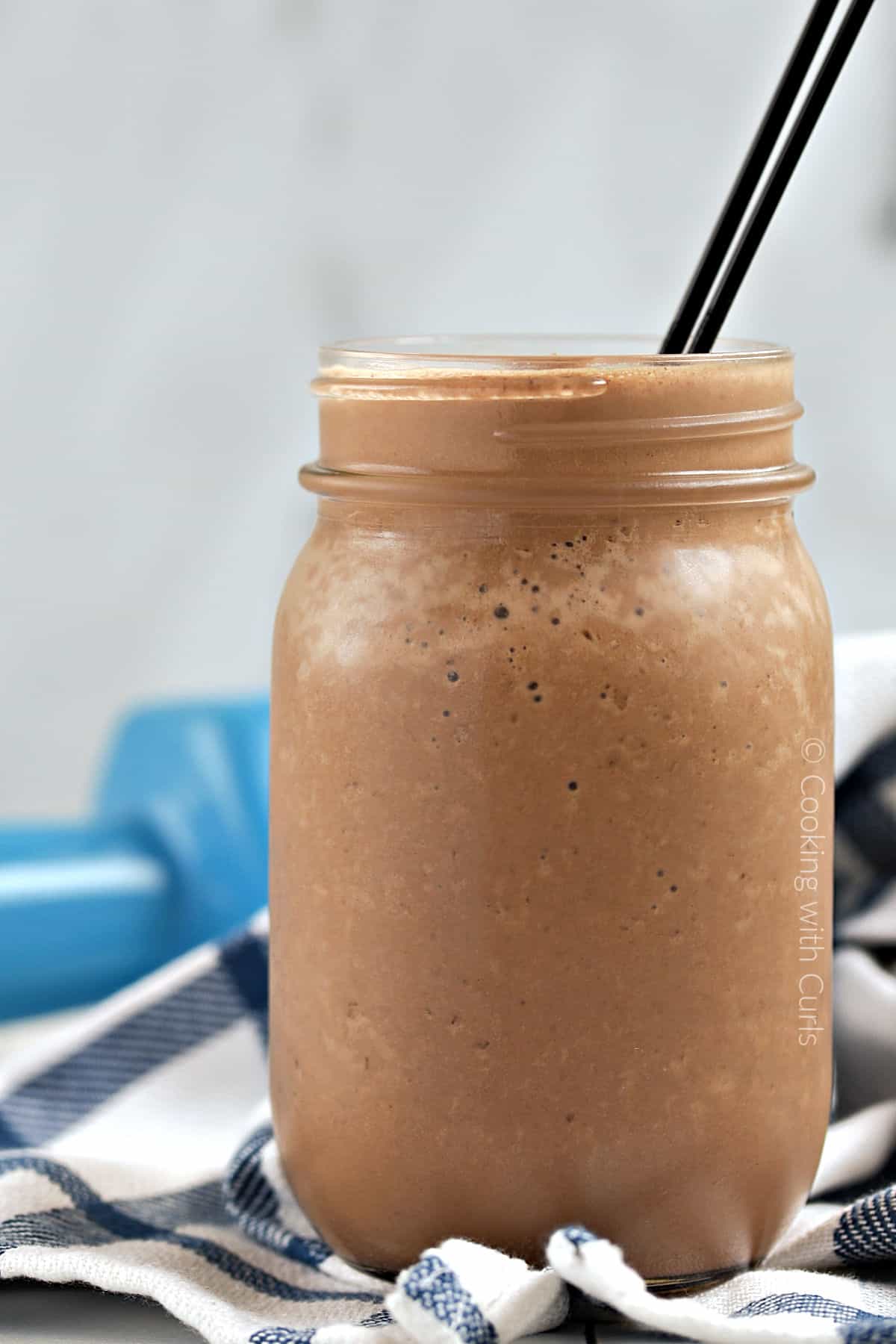 A thick chocolate smoothie in a glass jar with two thin straws sticking out of the top.