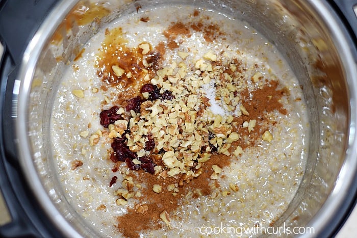 Cooked oatmeal in a pressure cooker with cinnamon, walnuts, cranberries. and agave nectar on top.