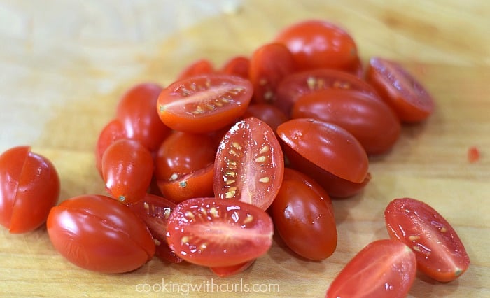 Cherry tomatoes sliced in half on a cutting board.