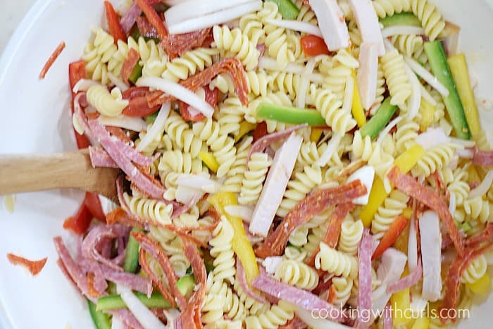 Sliced meats, bell peppers, and rotini pasta in a large white bowl.