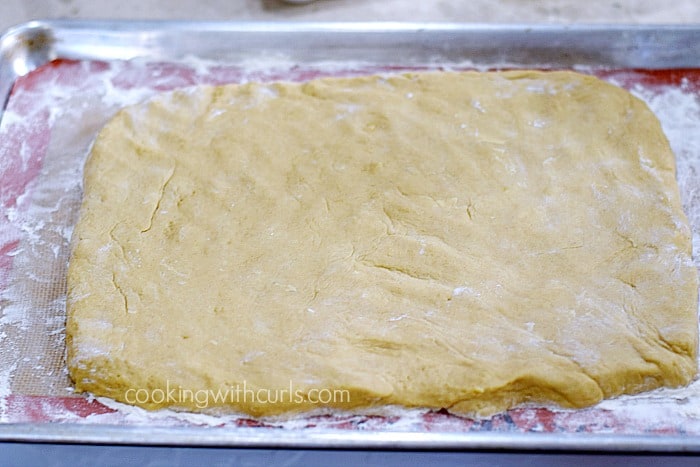 Doughnut batter flattened out into a rectangle on a silicone lined baking sheet.