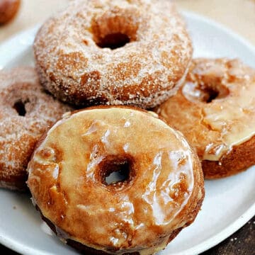 Five glazed and sugar coated apple cider doughnuts on a plate.
