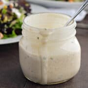 Chipotle Ranch Dressing in a short Mason jar with a spoon sticking up in the jar that's sitting in front of a plate of salad.