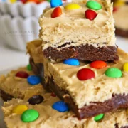 Whipped peanut butter topped brownies with candy coated candies on top.