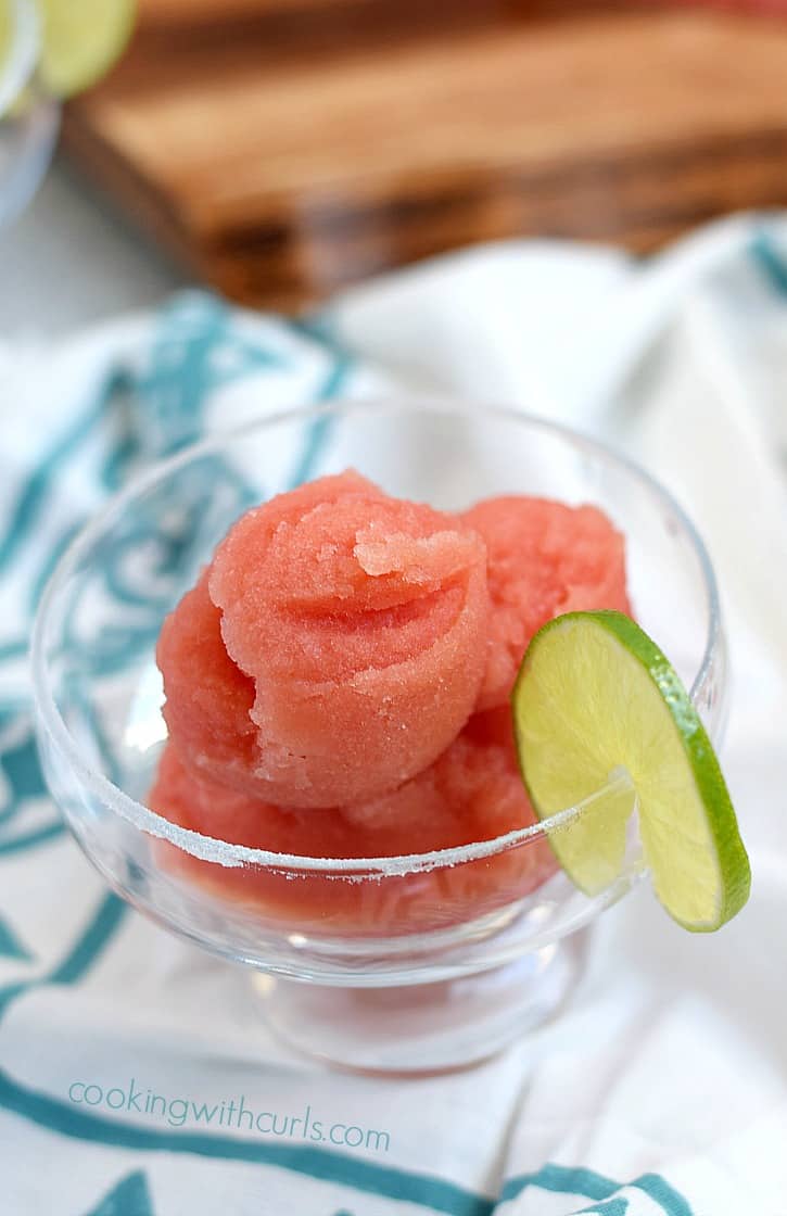 Small scoops of watermelon sorbet in a small dessert dish with a lime slice on the rim.