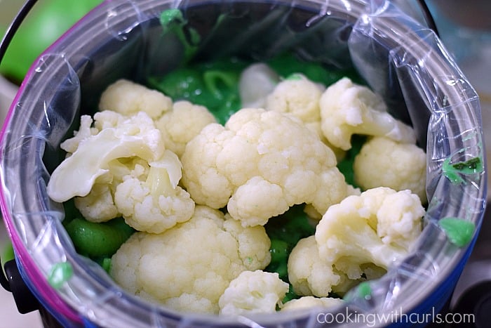 Cooked chunks of cauliflower sits on top of a layer of green macaroni and cheese in the paint can.