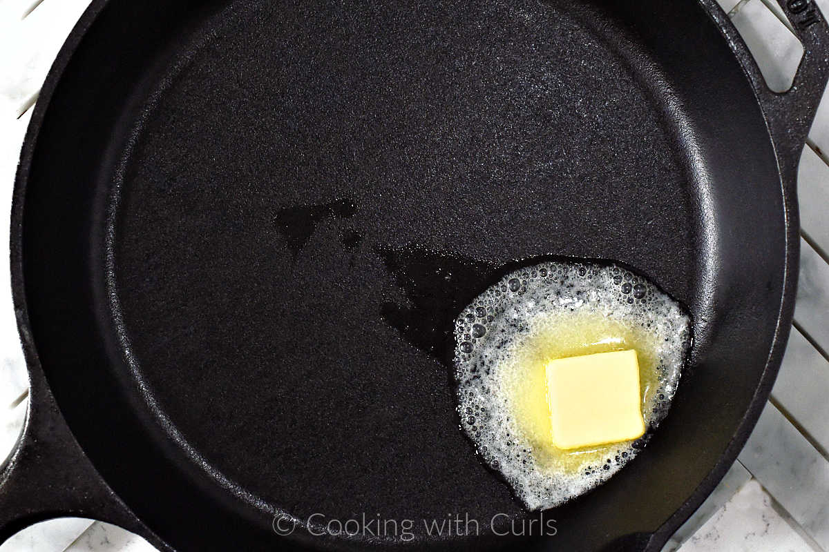 A pat of butter melting in a cast iron skillet.