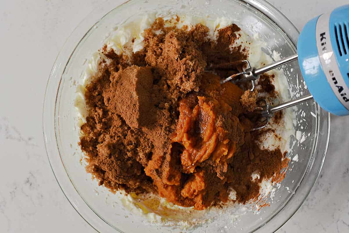 Pumpkin, sugar, spices, and cream cheese in a mixing bowl.