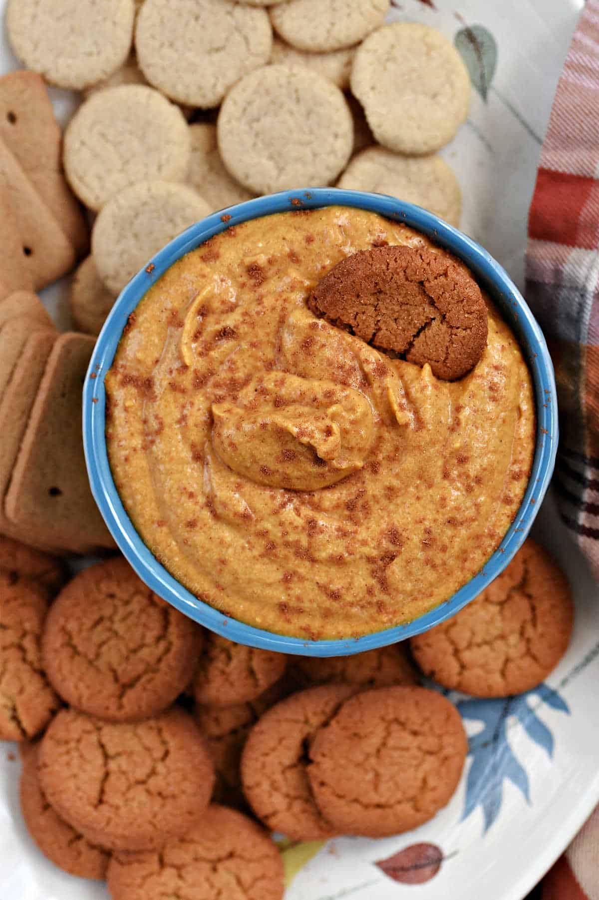A small bowl of creamy pumpkin dip sprinkled with spices and surrounded by three varieties of cookies.