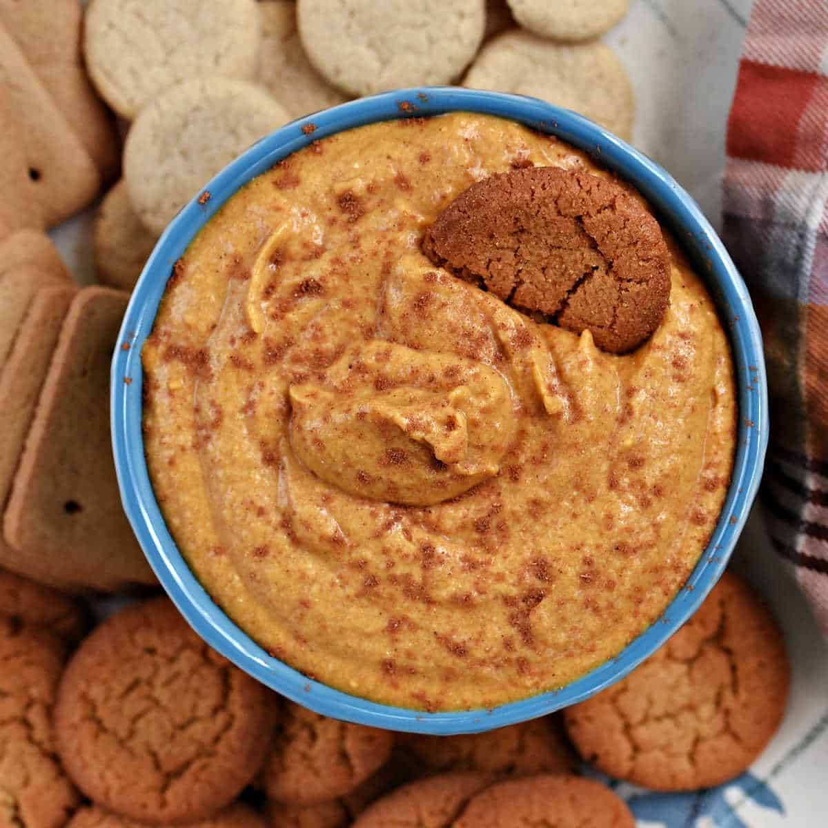 A bowl of creamy pumpkin dip sprinkled with spices and surrounded by cookies.