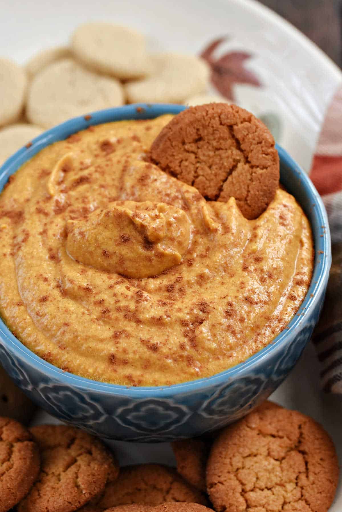 A bowl of creamy pumpkin dip sprinkled with spices and surrounded by cookies.