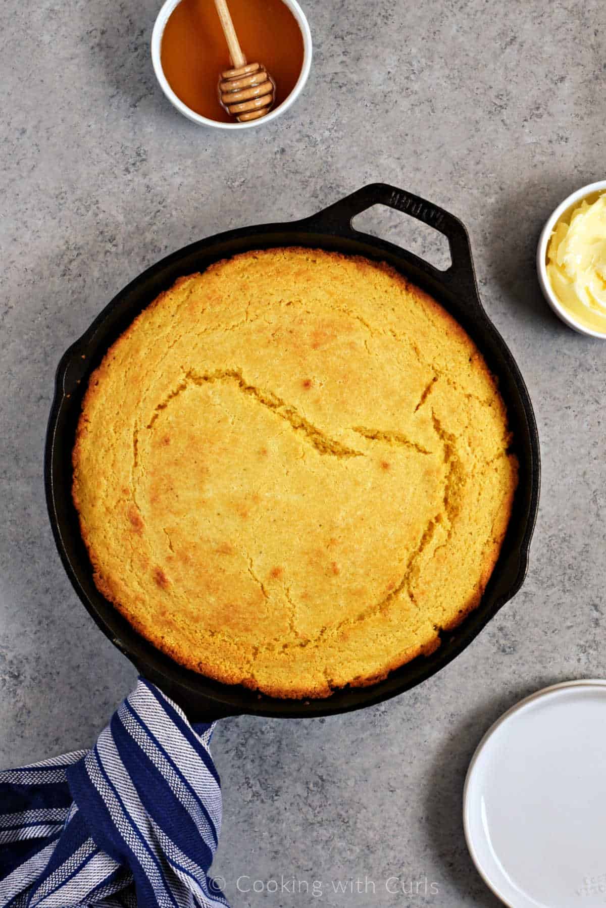 Looking down on a baked skillet cornbread with small bowls of honey and butter in the background.