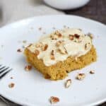 ! Pumpkin Spice Bar on a white plate with pecans and additional frosting in the background in small white bowls