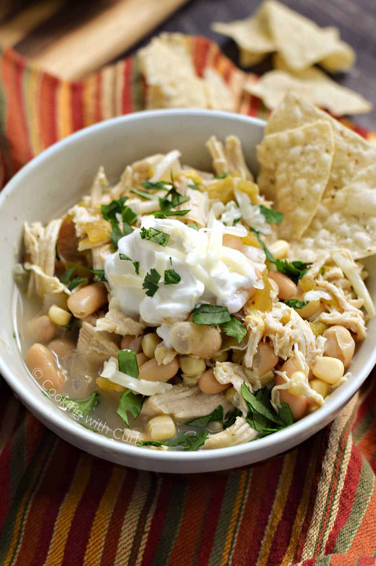 A bowl of white chili beans, shredded chicken, corn, and green chilies topped with sour cream, cilantro, and tortilla chips. 