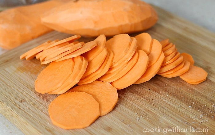 Peeled sweet potatoes and slices on a wooden cutting board.