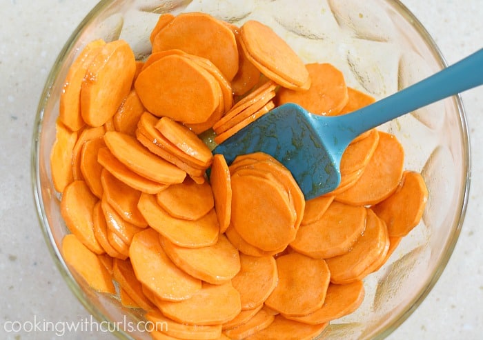 Sweet potato slices mixed with glaze in a glass bowl.