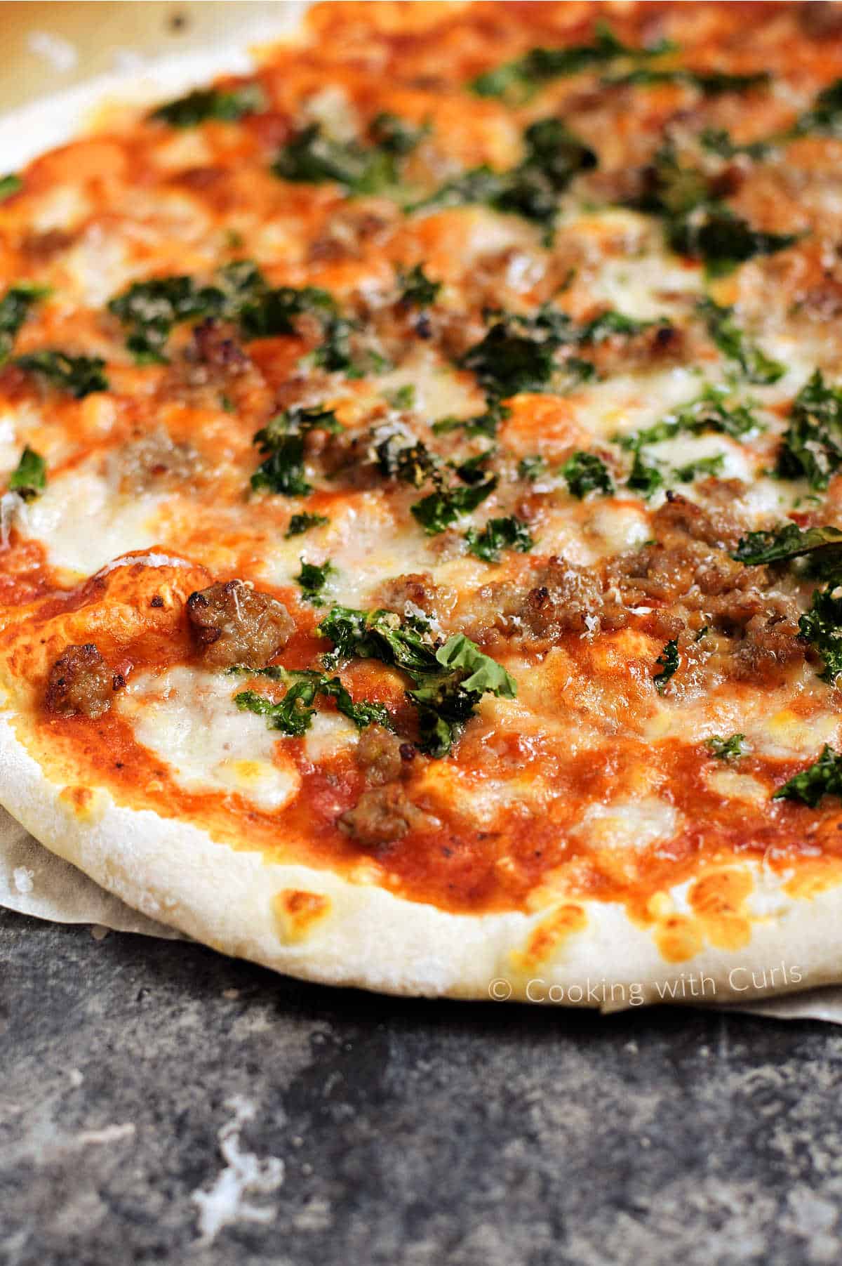 Close up image of a sausage and kale pizza on a sheet of parchment paper. 