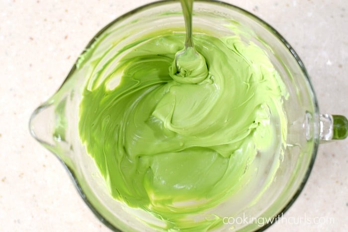 Melted green chocolate stirred together with a fork in a large mixing bowl.
