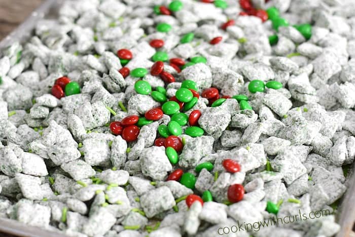 Grinch Puppy Chow and holiday candies mixed together on a baking sheet.