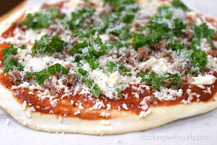 Pizza dough topped with sauce, grated mozzarella, chopped kale, crumbled Italian sausage, and grated parmesan.