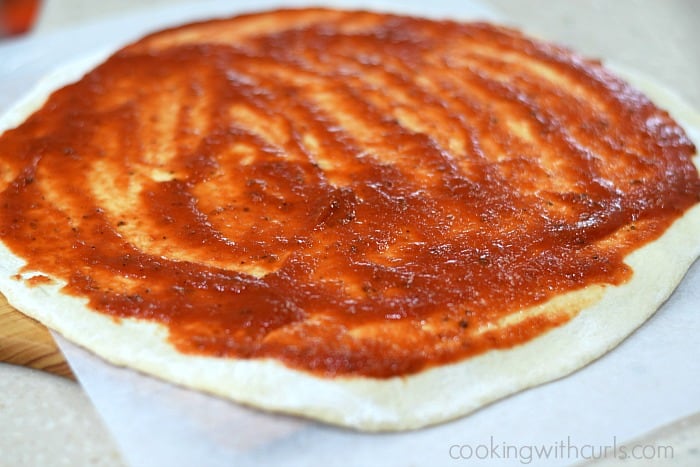 Red pizza sauce spread over a pizza dough circle.