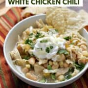 A bowl of white chili beans, shredded chicken, corn, and green chilies topped with sour cream, cilantro, and tortilla chips with title graphic across the top.
