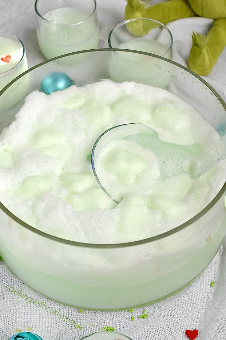 A glass punch bowl filled with bubbly lime green sherbet punch with a ladle in the center and filled glasses around the edge.