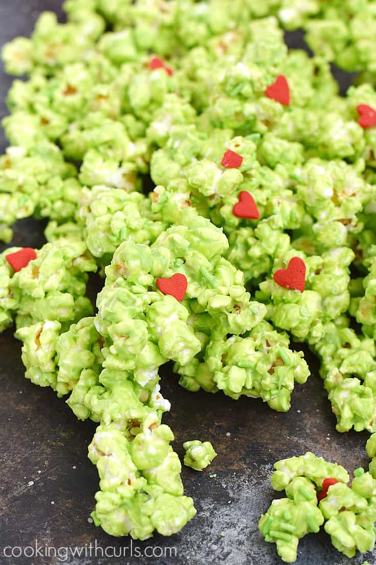 Green chocolate coated popcorn with candy pieces and red hearts spilled on a board.