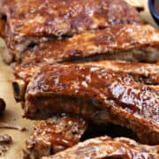A rack of bbq sauce coated pork spare ribs on a sheet of parchment paper.