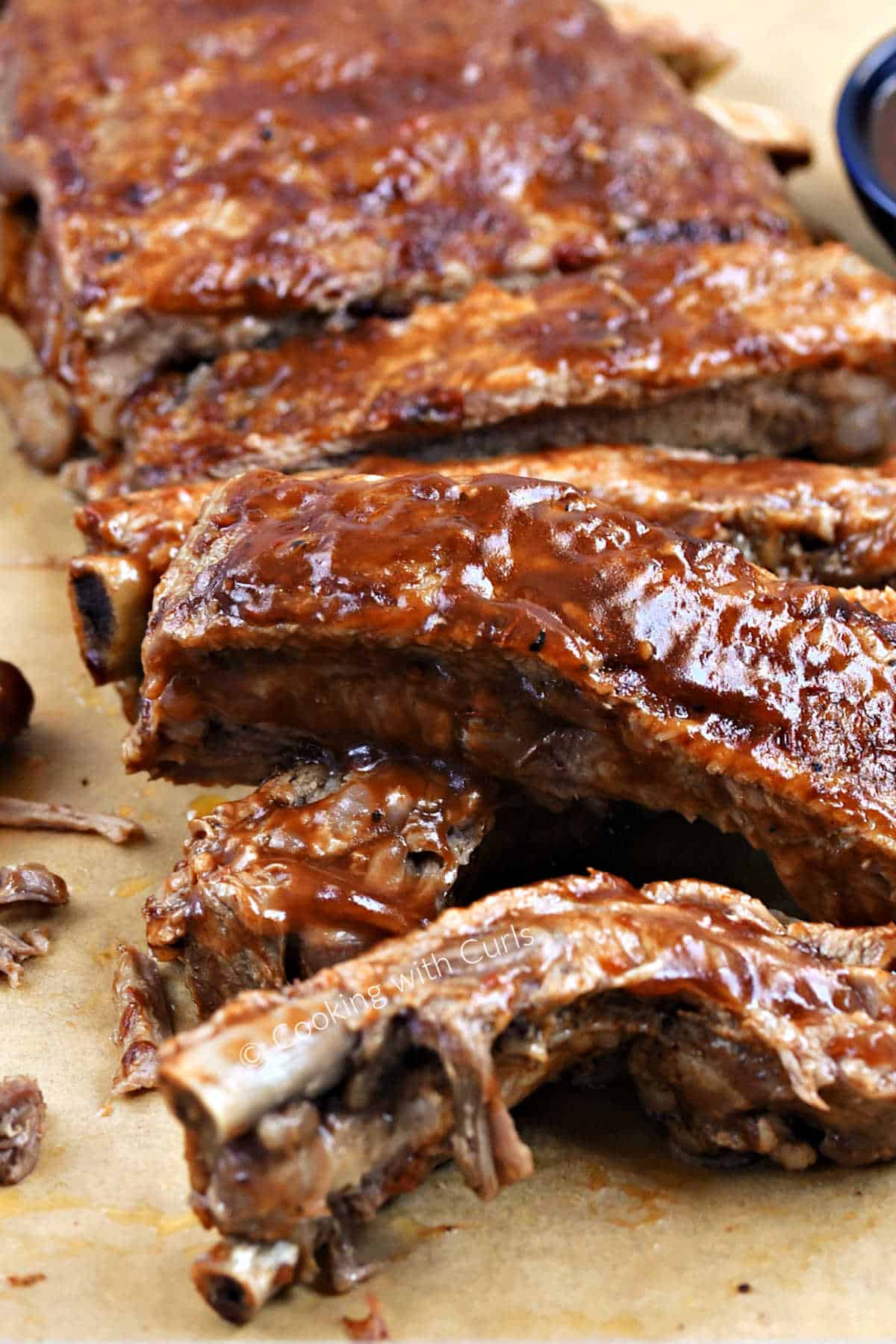 A rack of bbq sauce coated pork spare ribs on a sheet of parchment paper.
