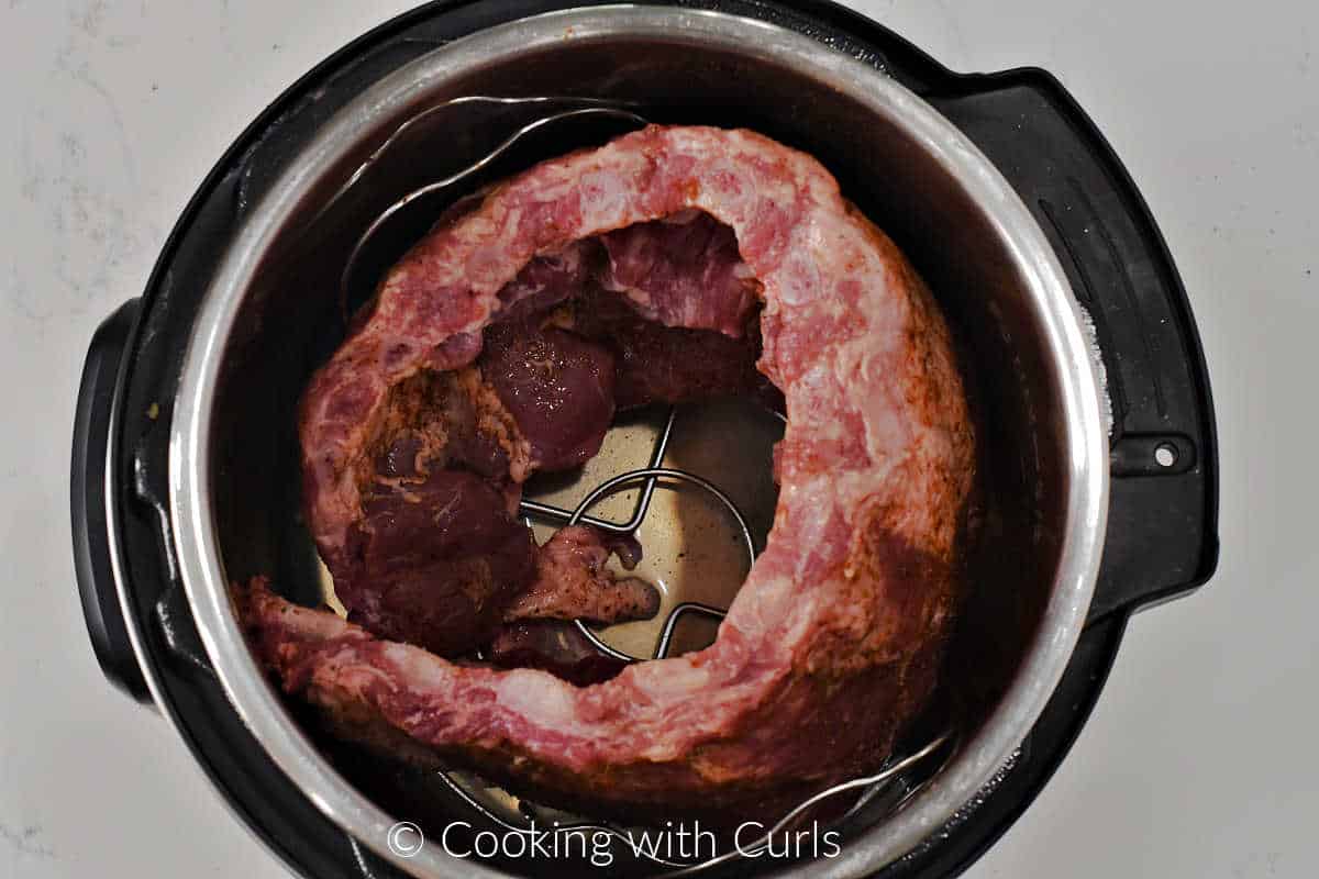 A rack of pork ribs coiled up in a pressure cooker on a trivet.