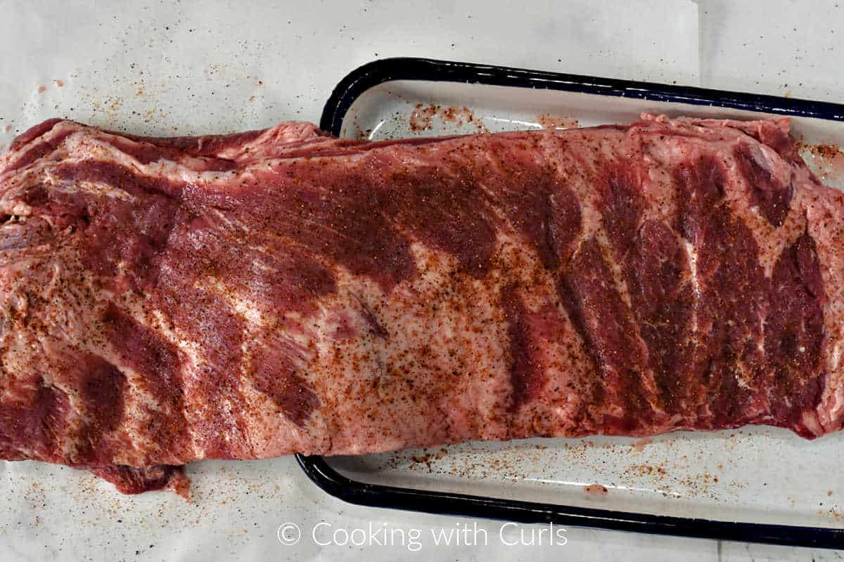 A seasoned rack of pork ribs on a tray.