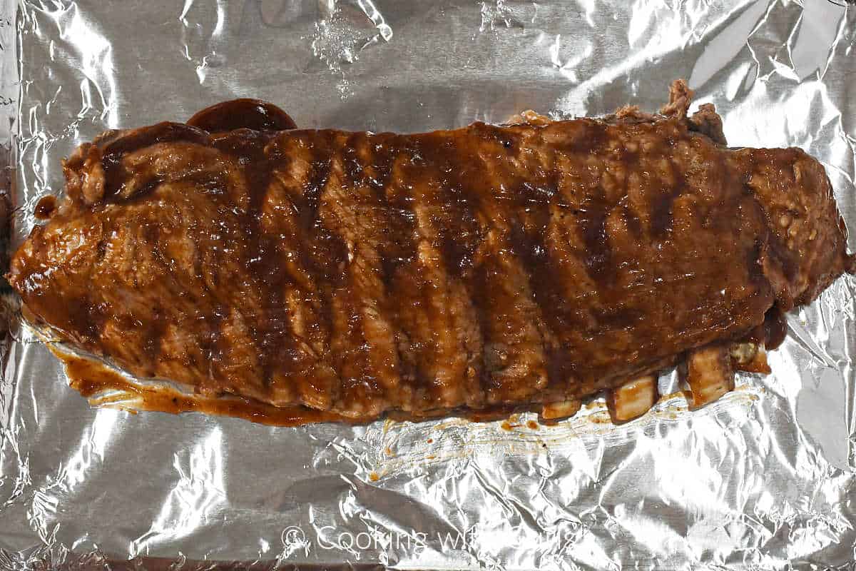 Barbecue sauce brushed over the cooked ribs on a foil lined baking sheet.