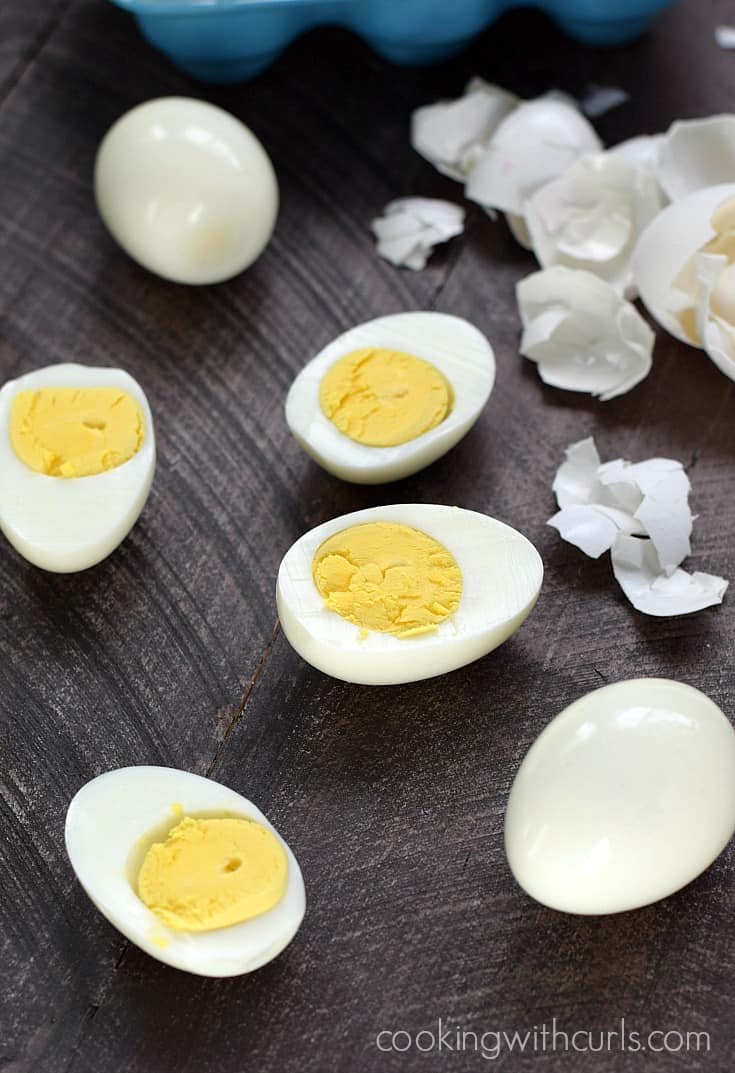 Hard Boiled Eggs on a board, some cut some whole surrounded by broken egg shells.