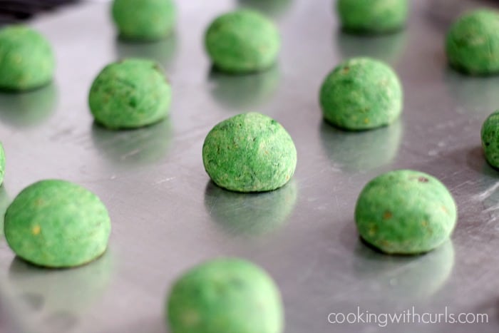 A tray of baked, green snowball cookies on a baking sheet.