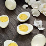 Two whole hard boiled eggs and two split in half surrounded by broken eggs shells.