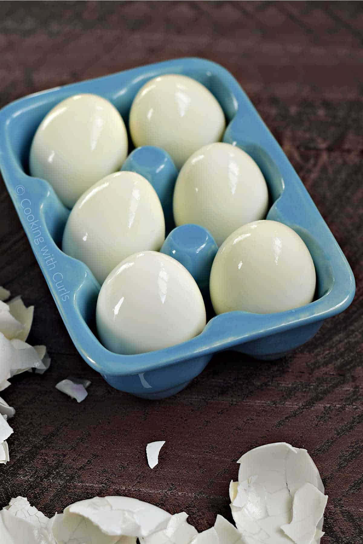 Six hard boiled eggs in a blue ceramic egg holder.