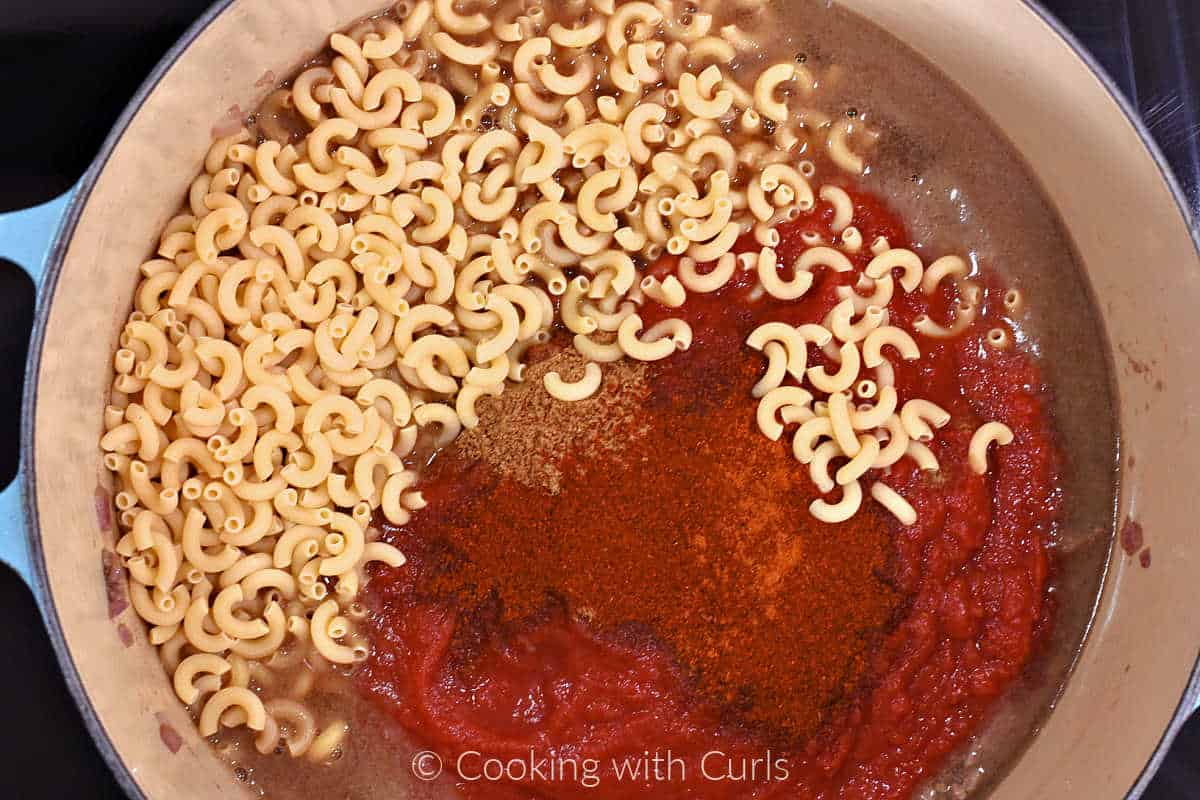 Uncooked macaroni, tomatoes, seasonings, and beef broth in a large pot.