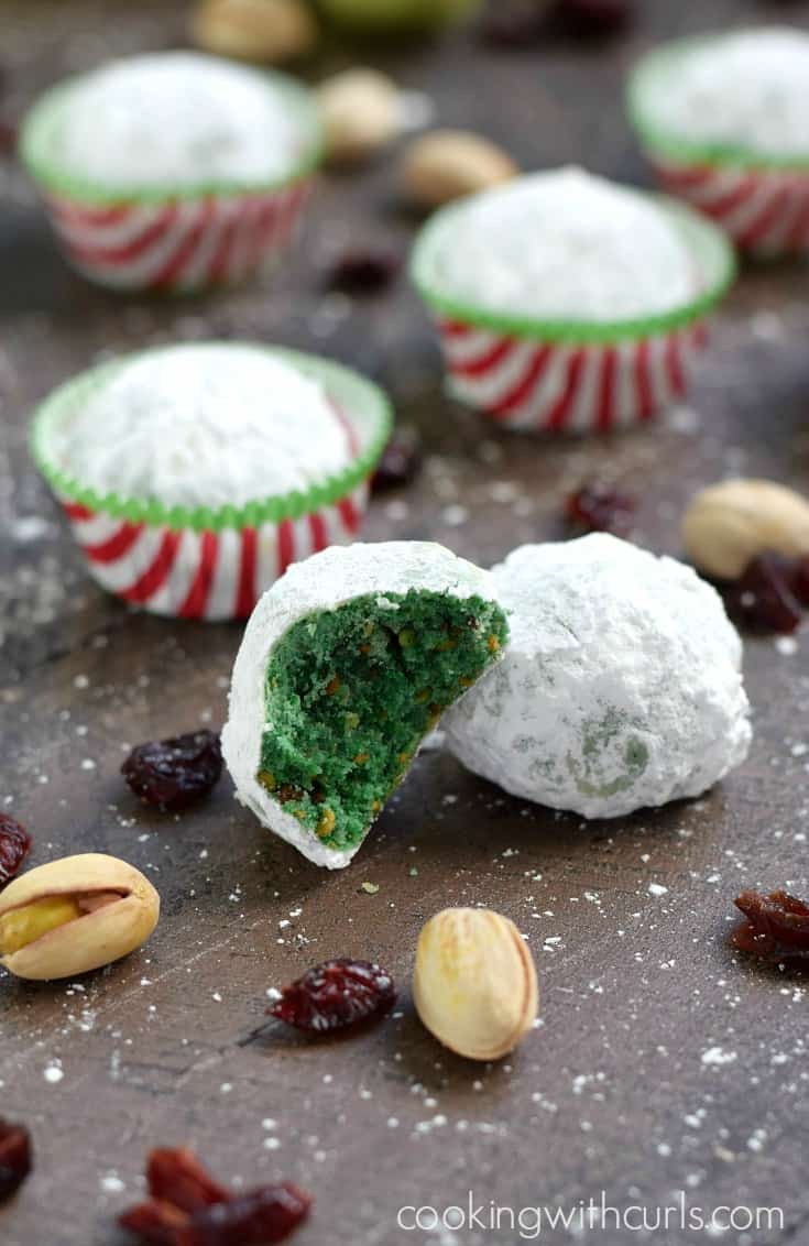 Four snowball cookies in red and white striped paper liners and two without surrounded by dried cranberries and pistachios.