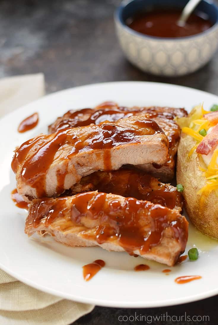 Barbecue Ribs topped with extra sauce with a loaded baked potato on the side.