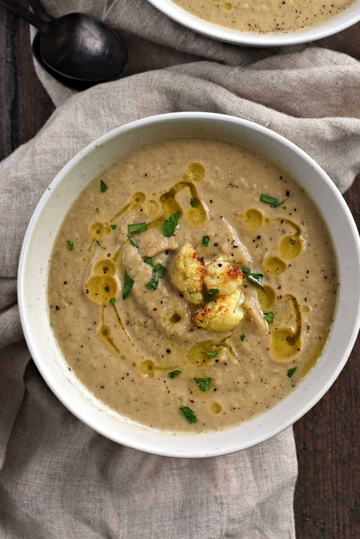 A bowl of roasted cauliflower and garlic soup drizzled with olive oil and crispy cauliflower pieces.