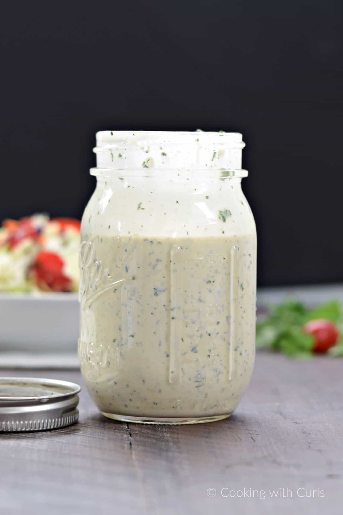 A jar of ranch dressing with a salad in the background.