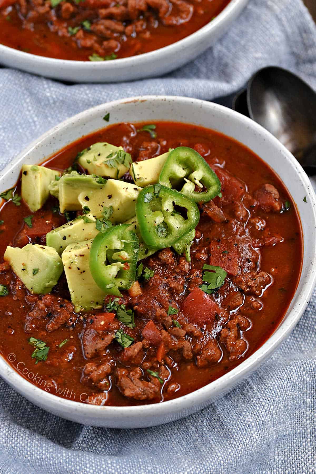 A bowl of bean-free chili in a bowl topped with avocado chunks and sliced jalapenos.