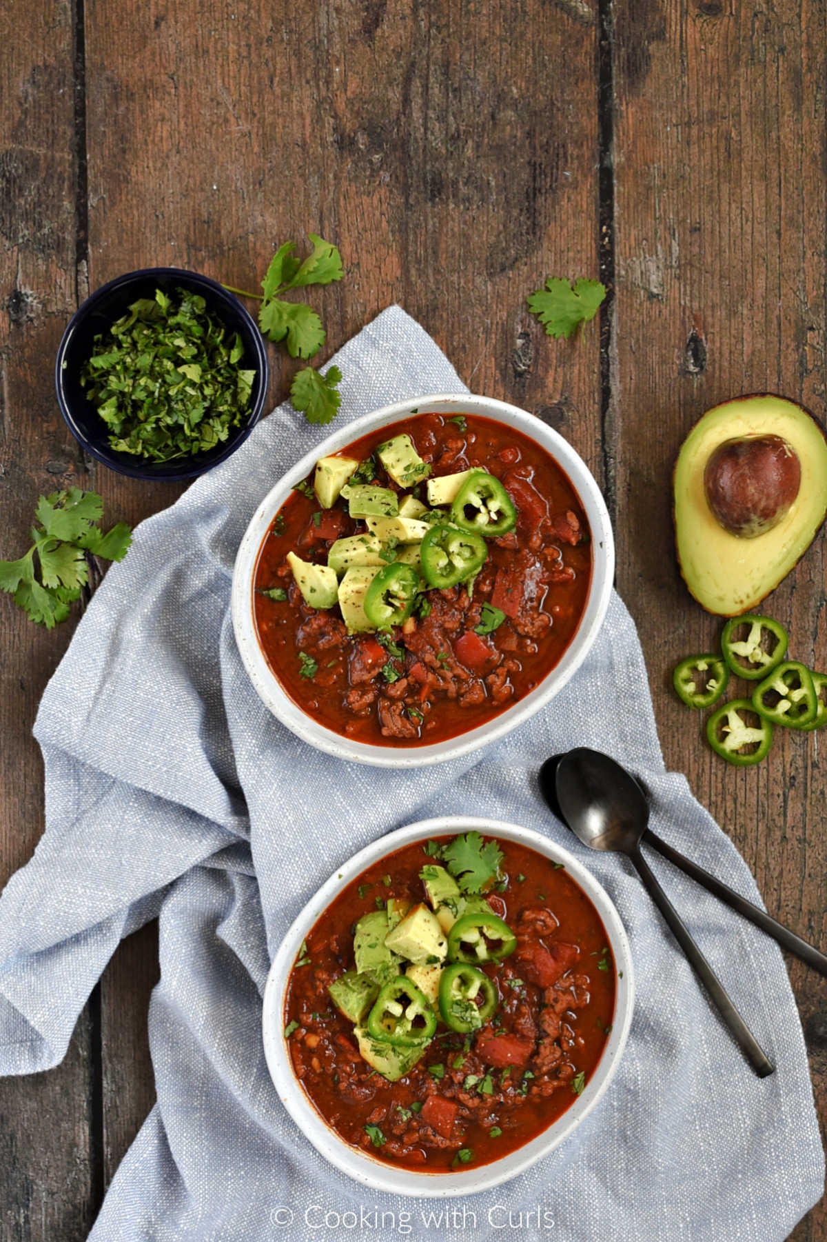 Looking down on two bowls of beanless chili topped with avocado and jalapeno slices.