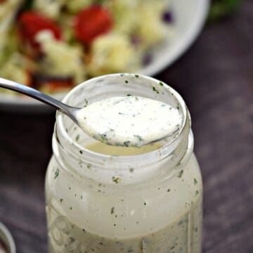 A spoon full of ranch dressing resting across the top of a jar full of dressing.