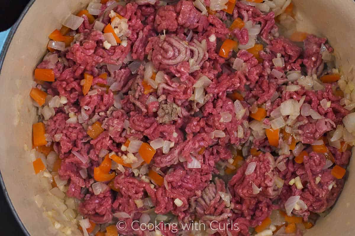 Ground beef stirred into the diced onion and bell pepper with a wood spatula.