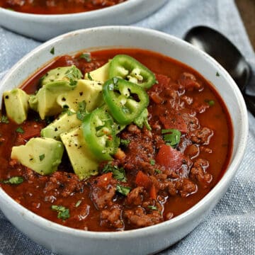 A bowl of bean-free chili in a bowl topped with avocado chunks and sliced jalapeno.